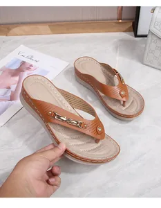 Detail of brown beach sandals with gold chain, rhinestone, and thick cream sole on marble