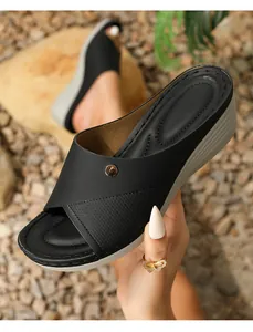 Detail of black wedge sandal featuring cross straps with gold buckle and micro-perforations