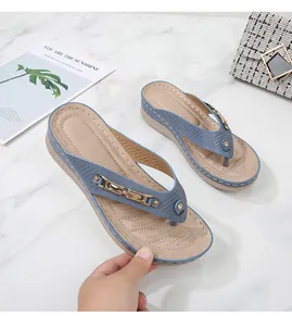 Detail of wedge flip flops featuring blue perforated straps and gold chain ornaments