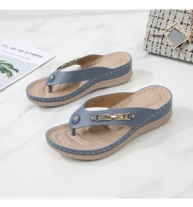 Detail of wedge thong sandals featuring perforated navy leather and gold buckle accents