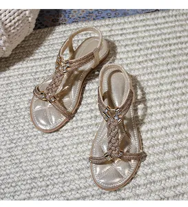 Κοντινό πλάνο χρυσών boho σανδαλιών με περίπλοκη ύφανση από στρας στο λουράκι T