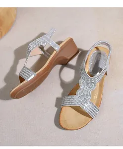 Dettaglio dei cinturini argentati con strass e cinturino elastico su sandali con zeppa