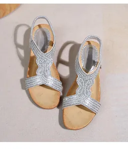 Dettaglio di sandali boho argentati con strass e cinturino elastico su tappetino beige