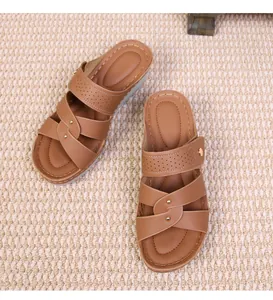 Detail view of brown wedge slippers with criss-cross straps and metallic studs on weave mat