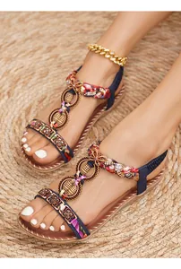 Dettaglio di sandali boho con strass, tessuto floreale e accenti dorati su una stuoia di paglia