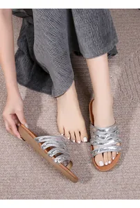 Detailed close-up of silver flat sandals with woven straps on a textured rug
