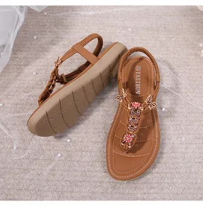 Detalle de sandalias T-strap marrones con mariposa de metal y adornos de strass rojos