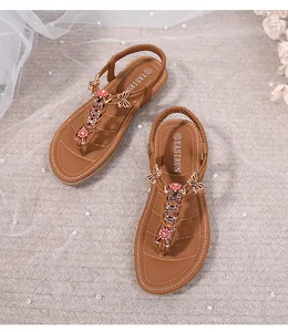 Detalle de sandalias planas marrones con mariposa de metal y flores de pedrería roja