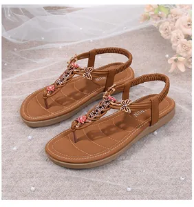 Detalle de sandalias de dedo marrones con mariposa de pedrería y flores rojas