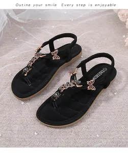 Detalle de sandalias negras con hebilla de mariposa dorada y pedrería negra para mujer