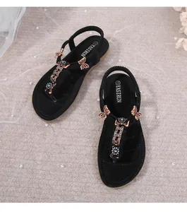 Detalle de sandalias planas negras con adornos de mariposas metálicas y flores de strass