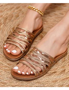 Flat gladiator sandals with metallic woven straps shown on a summer vacation straw mat