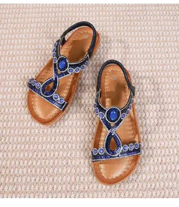 Détails des sandales bohèmes avec strass bleus et bride en T élastique sur tapis beige