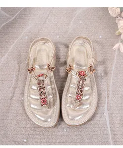 Detalle de sandalias planas doradas con flores de strass, mariposas de metal y tira elástica