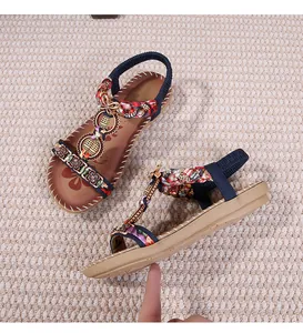 Dettaglio di sandali bohémien piatti con intrecci colorati, anelli metallici e fiori