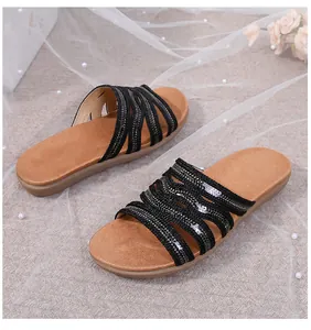 Detail of flat bohemian sandals featuring black sequined straps and brown cushioned sole