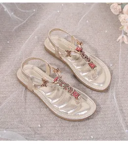 Detalle de sandalias planas doradas con mariposa de strass y adornos florales rojos