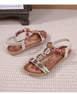 Dettaglio di sandali boho con cinturini intrecciati colorati e disco floreale perlato