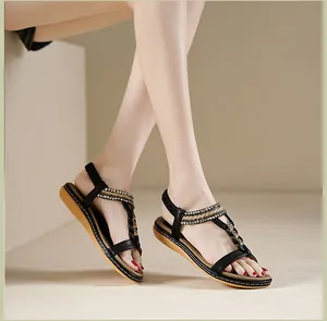Detail von schwarzen T-Steg Sandalen mit goldener Flechtoptik und glänzenden Strass