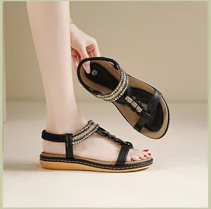 Detailaufnahme schwarzer Sandalen mit Strass-T-Riemen und goldenen Flechtakzenten
