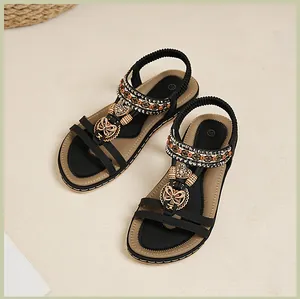 Détails de sandales noires plates avec perles bohèmes et breloques cœur dorées