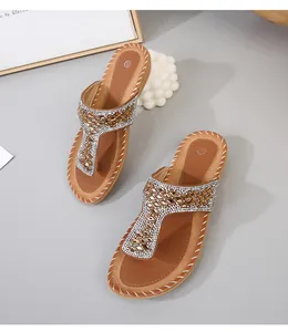 Detalle de sandalias planas bohemias con tira en T de diamantes y costuras blancas a mano