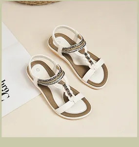 Detail weißer T-Steg Sandalen mit schwarz-goldener Perlenverzierung und elastischem Riemen