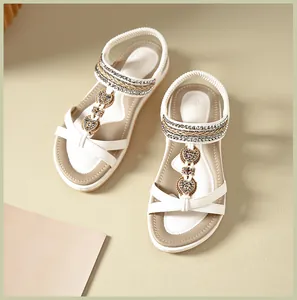Detail of white sandals featuring rhinestone T-straps and heart-shaped metal charms