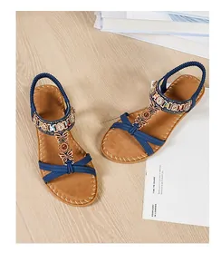 Flat bohemian sandals with rhinestone butterflies and beaded straps on a wooden surface