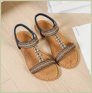Detalle de sandalias planas bohemias con tiras geométricas y adornos de cuentas metálicas