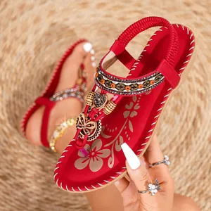 Detail van rode boho-sandalen met metalen vlinder, hartjeshanger en bloemenpatroon