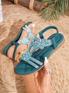 Dettaglio di sandali bassi bohémien con motivi floreali traforati e strass blu scintillanti