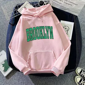 Close-up of pink hoodie with green Brooklyn print and pocket detail on flat lay