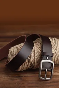Close-up of vintage dark brown leather belt with matte metal buckle on rustic wood surface