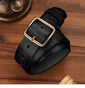 Détail d'une ceinture en cuir noir pour homme avec boucle en laiton vintage sur bois noir
