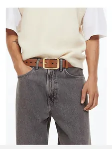 Dettaglio di cintura in pelle marrone con fibbia dorata su jeans in denim grigio lavato