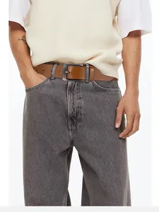Dettaglio cintura da uomo in pelle marrone con fibbia vintage in bronzo su jeans grigi