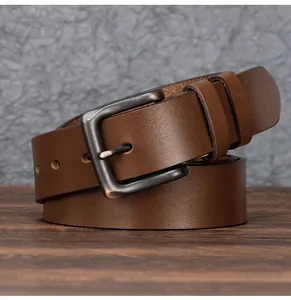 Gros plan d'une ceinture en cuir marron foncé avec boucle en bronze mat sur bois
