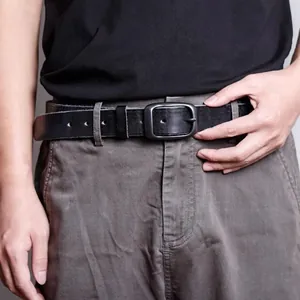 Close-up of a men's black leather belt with a dark grey matte buckle on grey trousers