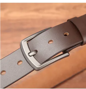 Detail of dark brown leather belt with matte gunmetal buckle on a wooden surface