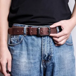 Detail of dark brown leather belt with vintage buckle on blue washed jeans
