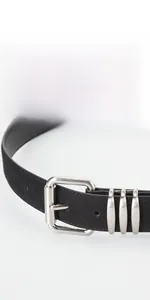 Détail d'une ceinture en daim noir montrant la boucle argentée et les trois anneaux en métal