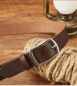 Dettaglio cintura in pelle marrone con fibbia in metallo su sfondo di legno vintage