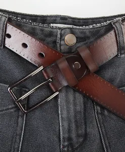 Detail of a dark brown leather belt with silver square buckle on vintage blue jeans