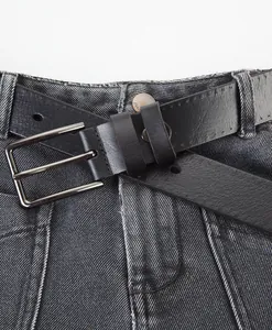 Detail view of black cowhide leather belt with silver alloy double-pin buckle on jeans