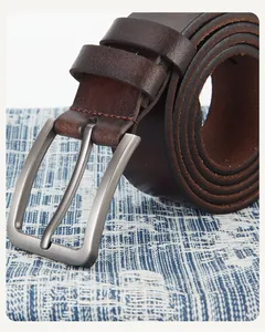 Détail de la ceinture en cuir marron avec boucle en métal mat et couture rouge