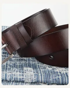 Détail d'une ceinture en cuir marron foncé avec boucle argentée mate sur fond bleu