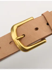 Dettaglio macro della cintura in pelle marrone con fibbia in ottone dorato opaco