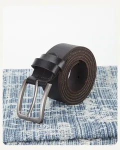 Détail d'une ceinture en cuir noir avec boucle ardillon en métal argenté brossé sur bleu