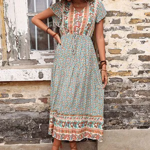 Bohemian floral maxi dress with V-neck and drawstring waist against a rustic wall background